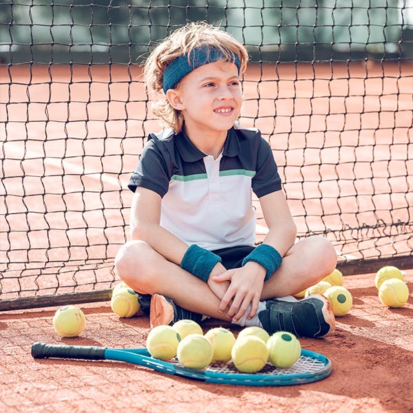 Jong meisje met racket bij het net, omringd door tennisballen