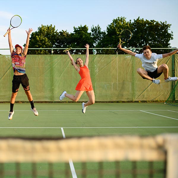 Drie volwassen spelers springen enthousiast op de tennisbaan